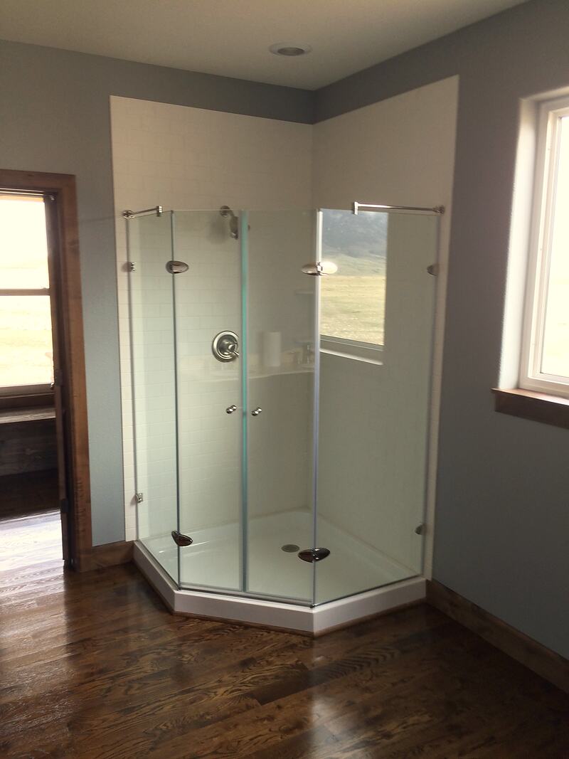 Bathroom corner shower with clear glass doors and white tile walls, next to a window that looks out on open grassland