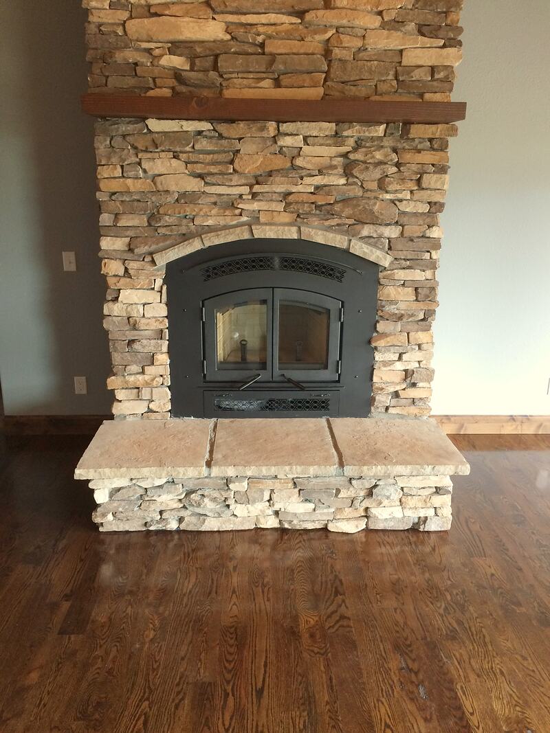 Stacked stone fireplace with a black arched insert, a wood mantel and a raised stone hearth on a dark hardwood floor