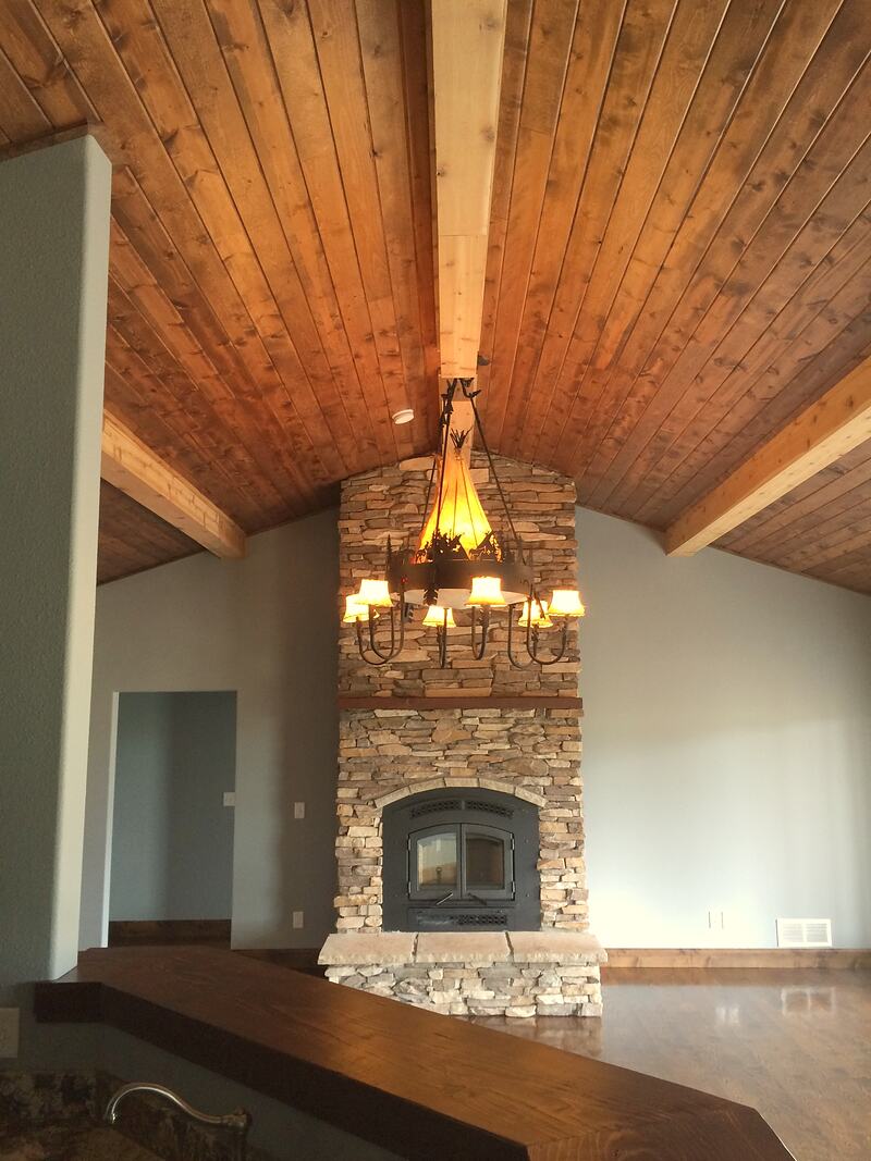 Great room with a stacked stone fireplace rising to a vaulted wood plank ceiling, an iron chandelier, and a wood-topped bar in the foreground
