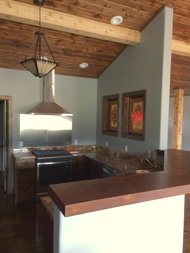 Kitchen corner with a range under a stainless steel hood and backsplash, stone counters, a pendant light, and two framed decorative glass panels on the wall