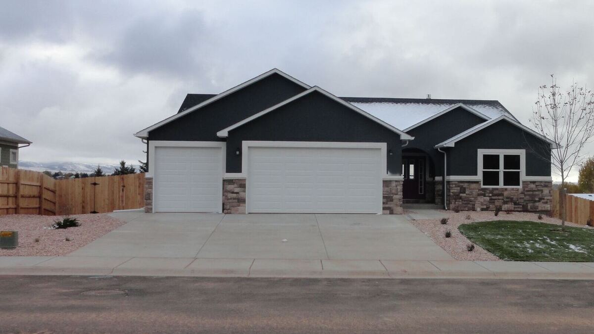 A single-story home built by Sheets Building & Contracting, with dark siding, a stone base and a three-car garage
