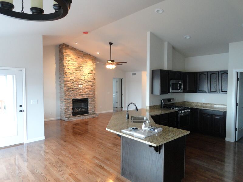 Great room and kitchen of a home built by Sheets Building & Contracting, with a stone fireplace, dark cabinets and a kitchen peninsula
