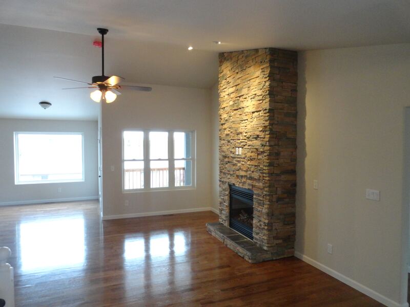 Living room of a home built by Sheets Building & Contracting, with a floor-to-ceiling stacked stone fireplace, wood floor and vaulted ceiling